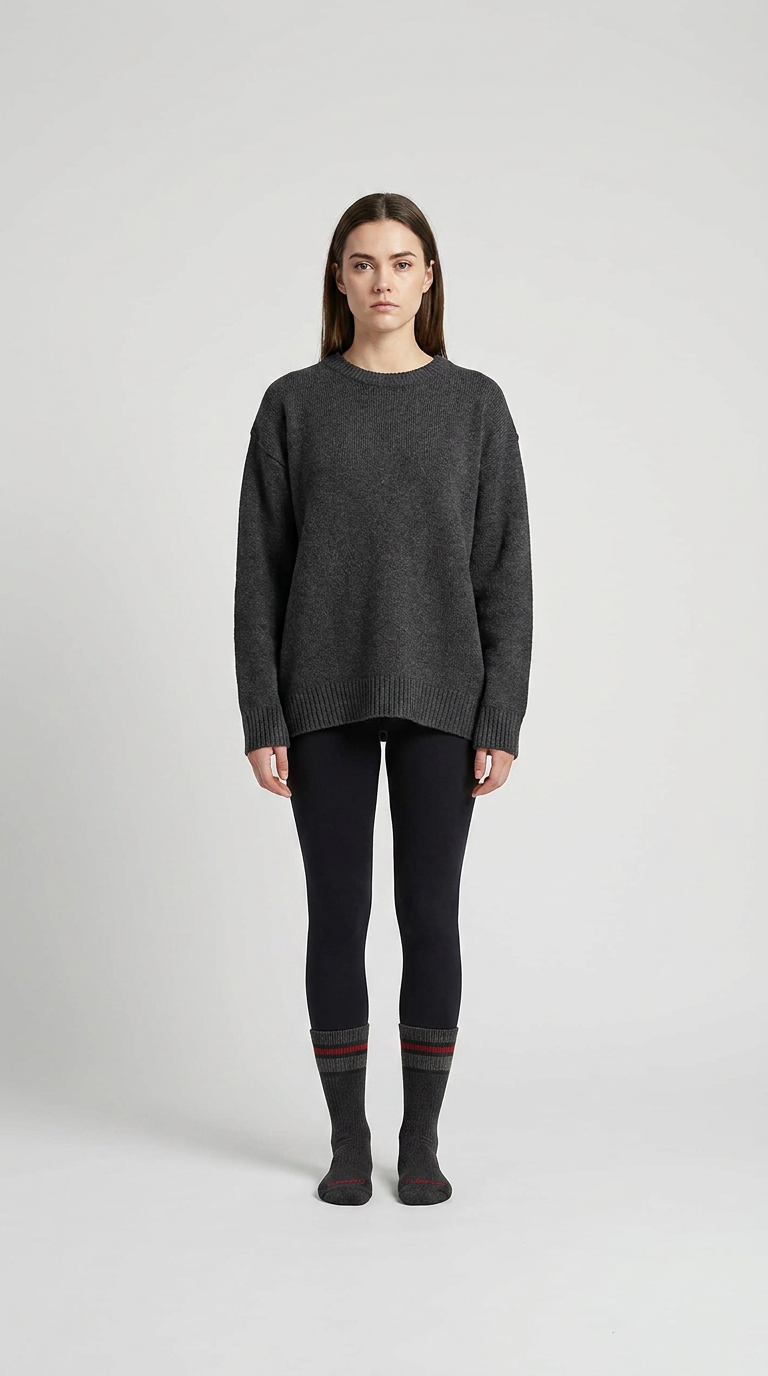Kvinde i en oversized grå striktrøje, sorte leggings og stribede sokker mod en lys baggrund.