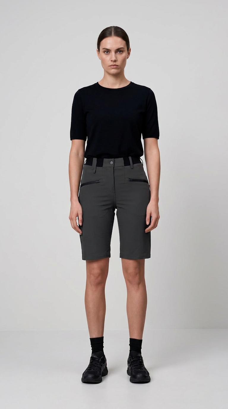 Kvinde iført sort t-shirt og mørkegrå shorts med lynlåslommer mod en lys baggrund.
