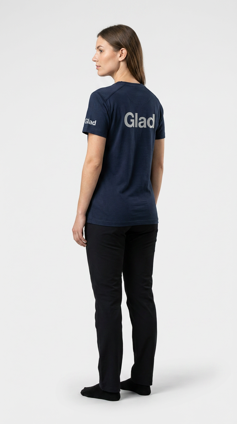 Kvinde set bagfra i mørkeblå t-shirt med "Glad" trykt på ryggen og sorte bukser mod en hvid baggrund.