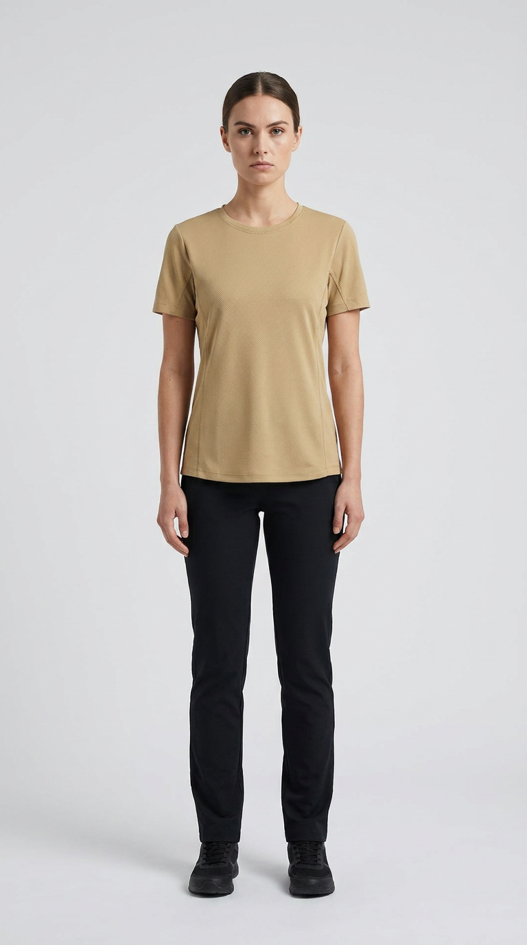 Kvinde i beige t-shirt og sorte bukser mod en lys grå baggrund.