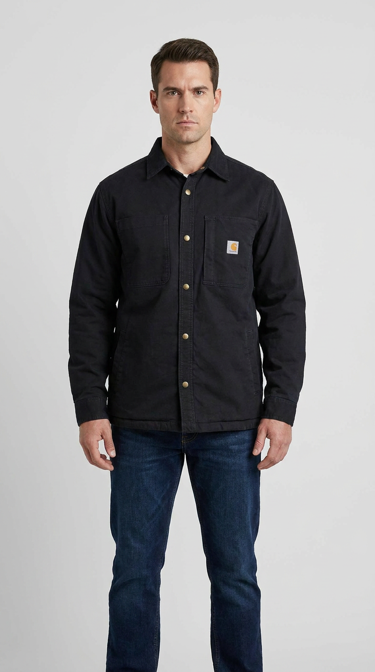 Mand iført en sort Carhartt skjortejakke med messingknapper og blå jeans på en grå baggrund.