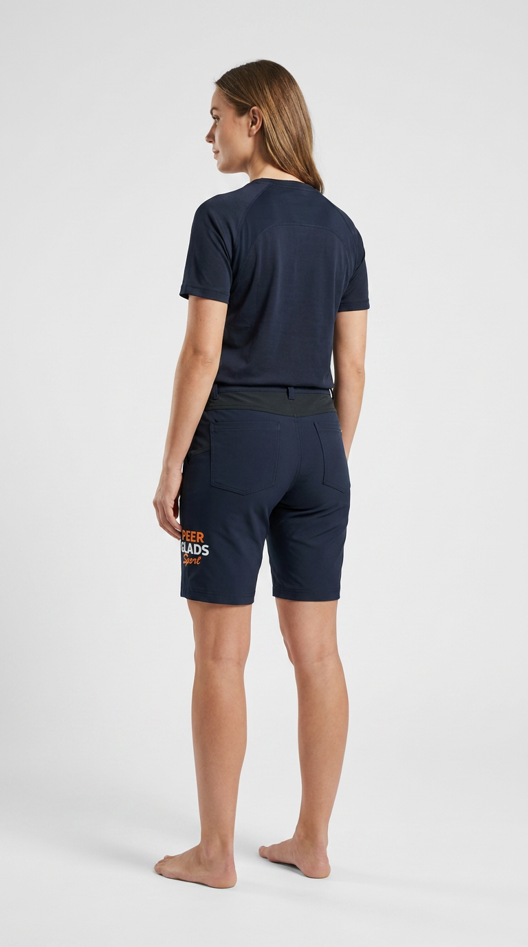 Kvinde set bagfra iført mørkeblå t-shirt og shorts med logo på benet mod en hvid baggrund.