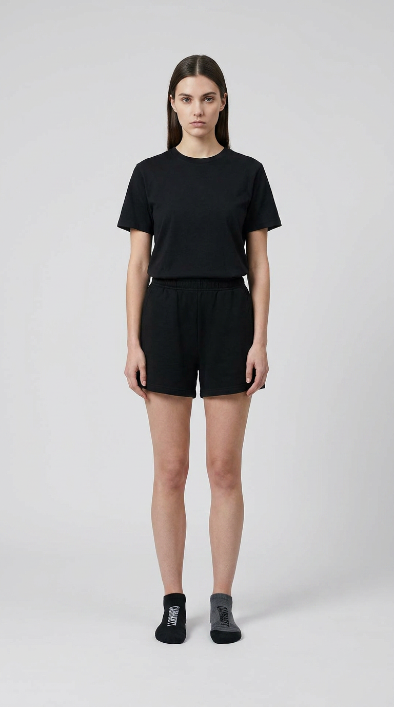 Kvinde i sort t-shirt og shorts med en sort og en grå sok foran en lys grå baggrund.