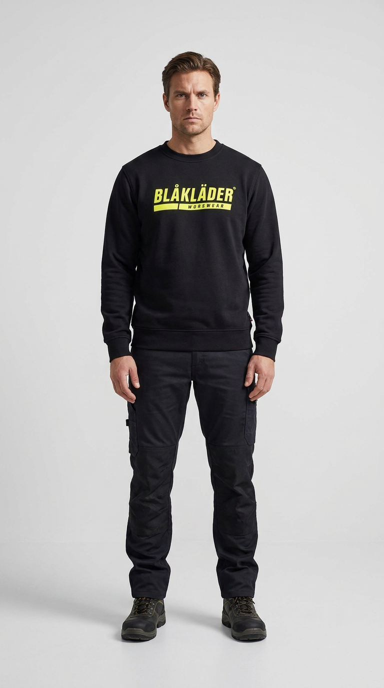 Mand i sort Blåkläder sweatshirt og sorte arbejdsbukser mod en grå baggrund.