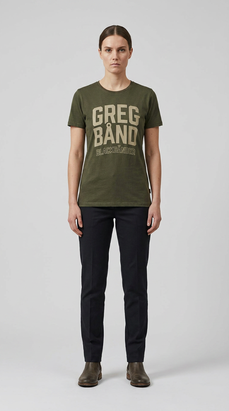 Kvinde i grøn t-shirt med "GREG BÅND" tekst, mørke bukser og støvler mod en grå baggrund.