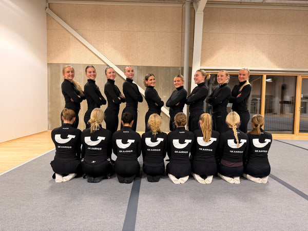 Gymnaster fra GK Aarhus i ens sorte sportstrøjer med logo stillet op i hallen