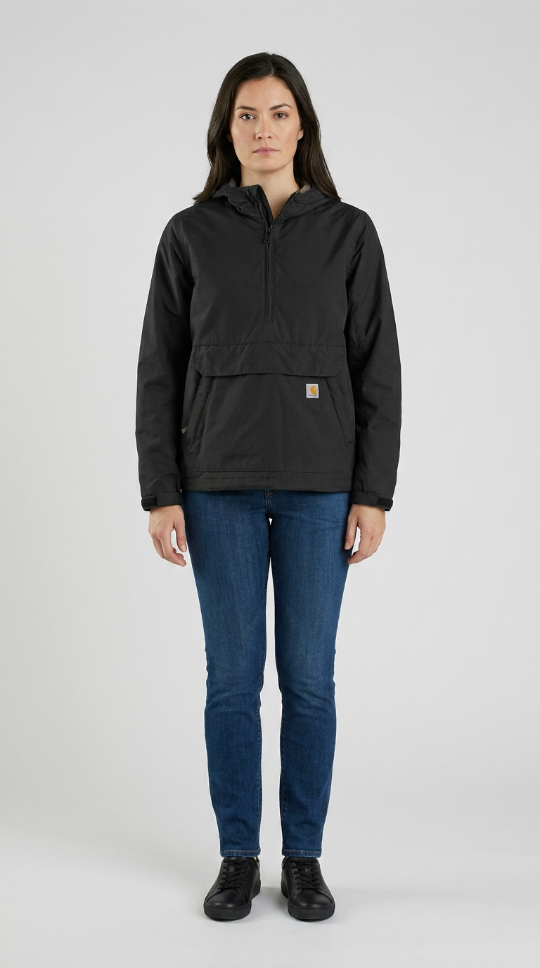 Kvinde iført en sort Carhartt anorak og blå jeans mod en enkel grå baggrund.