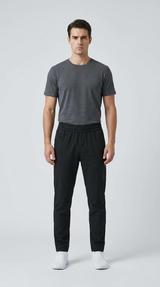 Mand iført mørkegrå t-shirt, sorte bukser og hvide sneakers mod en lys baggrund.
