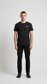 Mand i sort t-shirt med lille logo og sorte jeans stående mod en hvid baggrund.