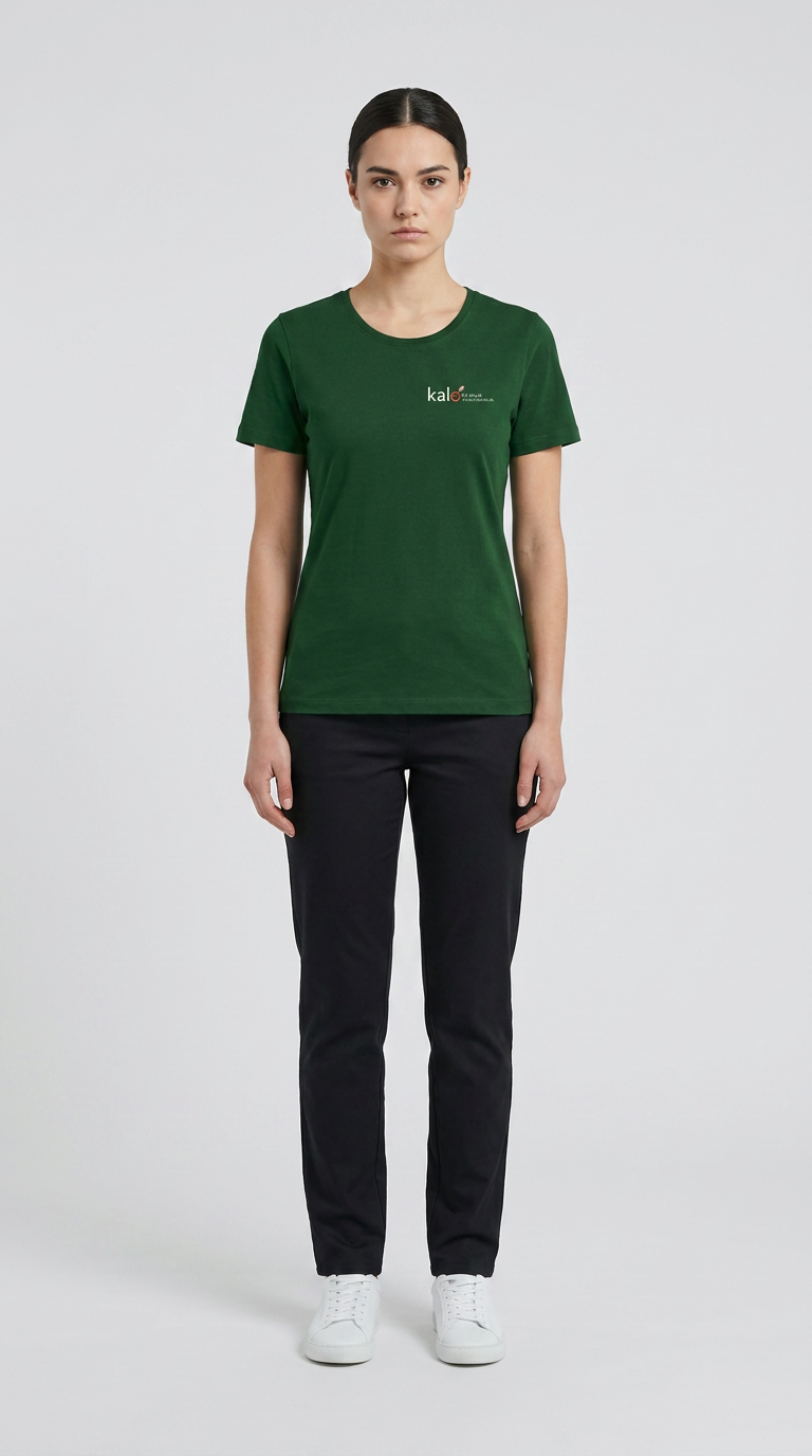 Kvinde iført grøn t-shirt med logo, sorte bukser og hvide sneakers på en lys grå baggrund.