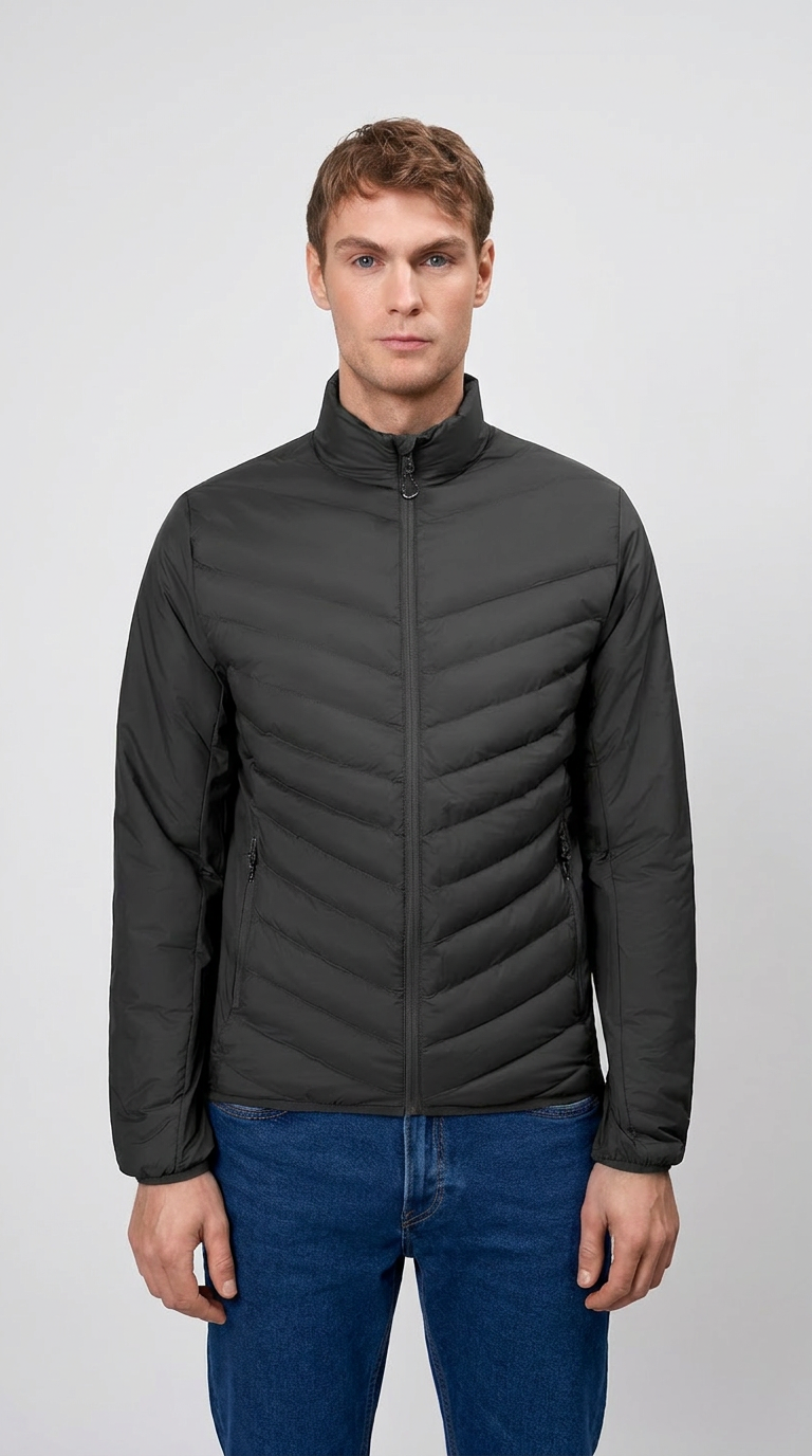 Mand iført en sort quiltet overgangsjakke og blå jeans mod en neutral baggrund.