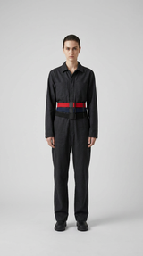 Model i mørkegrå jumpsuit med tre bælter i rød, blå og sort mod en neutral grå baggrund.