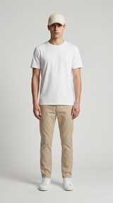 Mand iført hvid t-shirt, beige bukser, hvide sneakers og en kasket mod en lys baggrund.