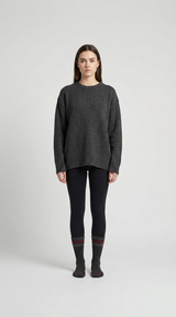 Kvinde i en oversized grå striktrøje, sorte leggings og stribede sokker mod en lys baggrund.