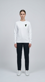 Kvinde i hvid sweatshirt med lille logo, mørke bukser og hvide sneakers mod en lys grå baggrund.