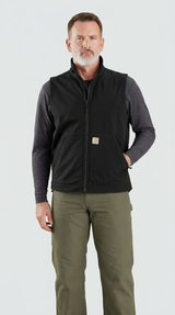 Mand i sort Carhartt-vest, grå trøje og grønne bukser foran en hvid baggrund.
