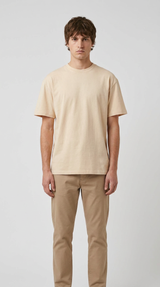 Mand iført en beige t-shirt og khaki bukser mod en grå baggrund.