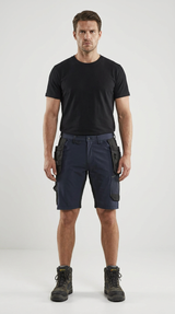 Mand iført sort t-shirt, mørkeblå arbejdsshorts med værktøjslommer og robuste støvler.