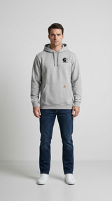 En mand i en grå Carhartt-hættetrøje, blå jeans og hvide sneakers foran en enkel grå baggrund.