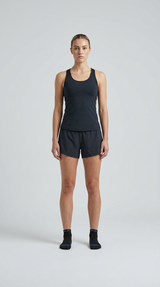 Kvinde i sort tanktop og shorts stående mod en lys baggrund.