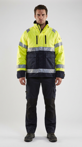 Mand i gul og mørkeblå high-visibility arbejdsjakke med reflekser og matchende bukser på en lys baggrund.