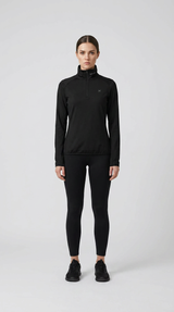Kvinde i sort langærmet træningstrøje med lynlås og sorte leggings mod en lys baggrund.