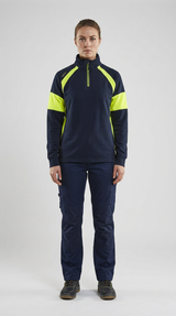 Kvinde i mørkeblå sweatshirt med neon-gule paneler og mørkeblå arbejdsbukser mod en hvid baggrund.