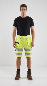 Mand i sort t-shirt og neon-gule high-vis arbejdsshorts med refleksstriber og brune støvler.