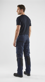 Mand i mørkeblå arbejdsbukser med sorte forstærkninger og t-shirt set bagfra mod hvid baggrund.