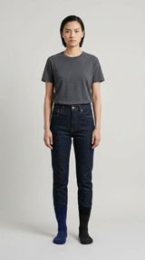 Kvinde i mørkegrå t-shirt og mørkeblå jeans med en blå og en sort sok mod en lys grå baggrund.