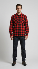 En mand i en rød og sort ternet skovmandsskjorte, mørkeblå jeans og brune støvler mod en grå baggrund.