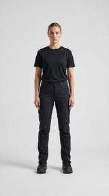 Kvinde iført sort t-shirt og sorte outdoorbukser stående mod en lys baggrund.