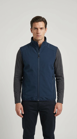 Mand iført en mørkeblå softshell-vest, grå trøje og mørke bukser foran en lys grå baggrund.