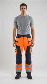 Mand i grå t-shirt og orange hi-vis arbejdsbukser med reflekser mod en lys baggrund.
