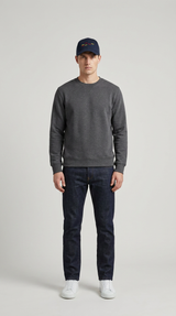 Mand iført mørkegrå sweatshirt, mørkeblå jeans, hvide sneakers og kasket på en lys grå baggrund.