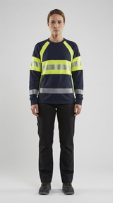 Kvinde i mørkeblå sweatshirt med gule high-vis detaljer, refleksstriber og sorte arbejdsbukser på grå baggrund.