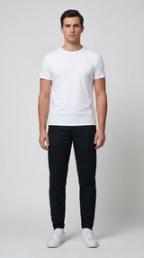 Mand i hvid t-shirt og sorte bukser med hvide sneakers på en lys baggrund.
