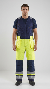 Mand i mørkeblå arbejdsvest og fluorescerende gule og mørkeblå arbejdsbukser med refleksstriber.
