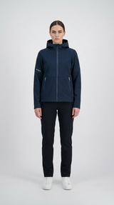 Kvinde i mørkeblå softshell-jakke med hætte, sorte bukser og hvide sneakers på en hvid baggrund.