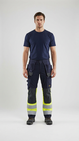 Mand i mørkeblå t-shirt og arbejdsbukser med knæpuder og high-visibility detaljer.