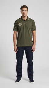 Mand i olivengrøn polo-shirt og mørkeblå cargobukser mod en lys baggrund.