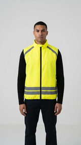 Mand iført en neongul sikkerhedsvest med refleksstriber over en sort langærmet trøje.