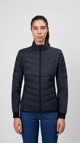 Kvinde iført en mørkeblå quiltet hybridjakke og blå jeans mod en lys grå baggrund.