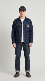 Mand iført mørkeblå denimjakke, jeans, sort kasket og brune støvler foran en grå baggrund.