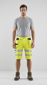 Mand i grå t-shirt, neongule arbejdsshorts med refleksstriber og arbejdsstøvler.