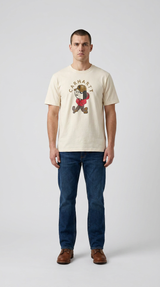 Mand i cremehvid Carhartt t-shirt med tegneserieprint, blå jeans og brune støvler mod en hvid baggrund.