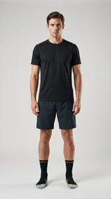 Mand i sort t-shirt, mørke shorts og sorte sportssokker mod en neutral grå baggrund.