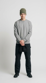 Mand i grå sweatshirt, sorte bukser og olivengrøn hue, der holder en sort hat mod en hvid baggrund.