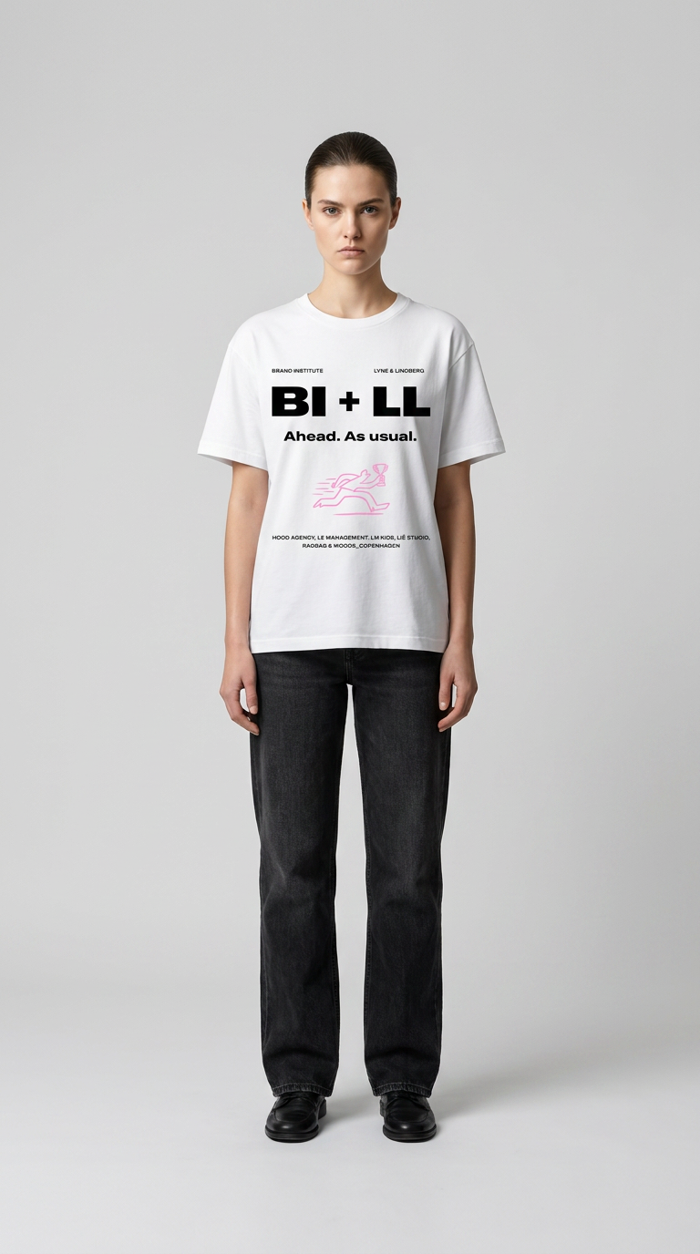Kvinde i hvid grafisk t-shirt og sorte jeans stående mod en grå baggrund.