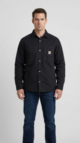 Mand iført en sort Carhartt skjortejakke med messingknapper og blå jeans på en grå baggrund.